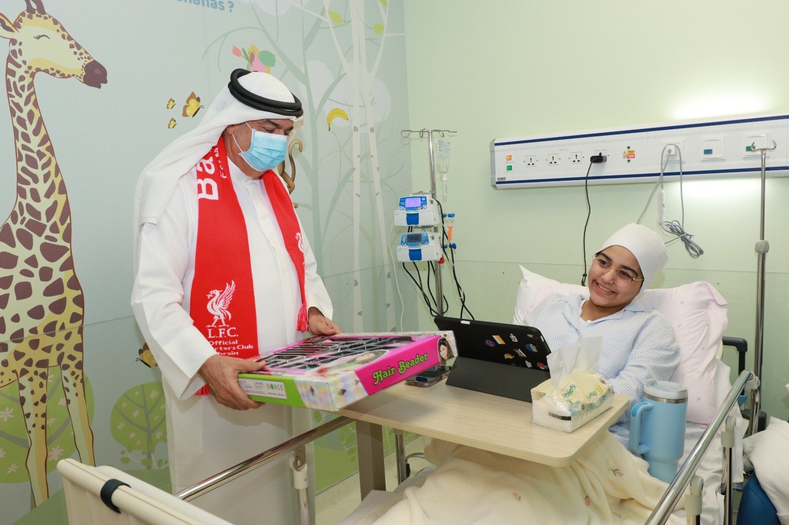OLSC Bahrain representative presenting a boxed gift to a young person in a hospital room.
