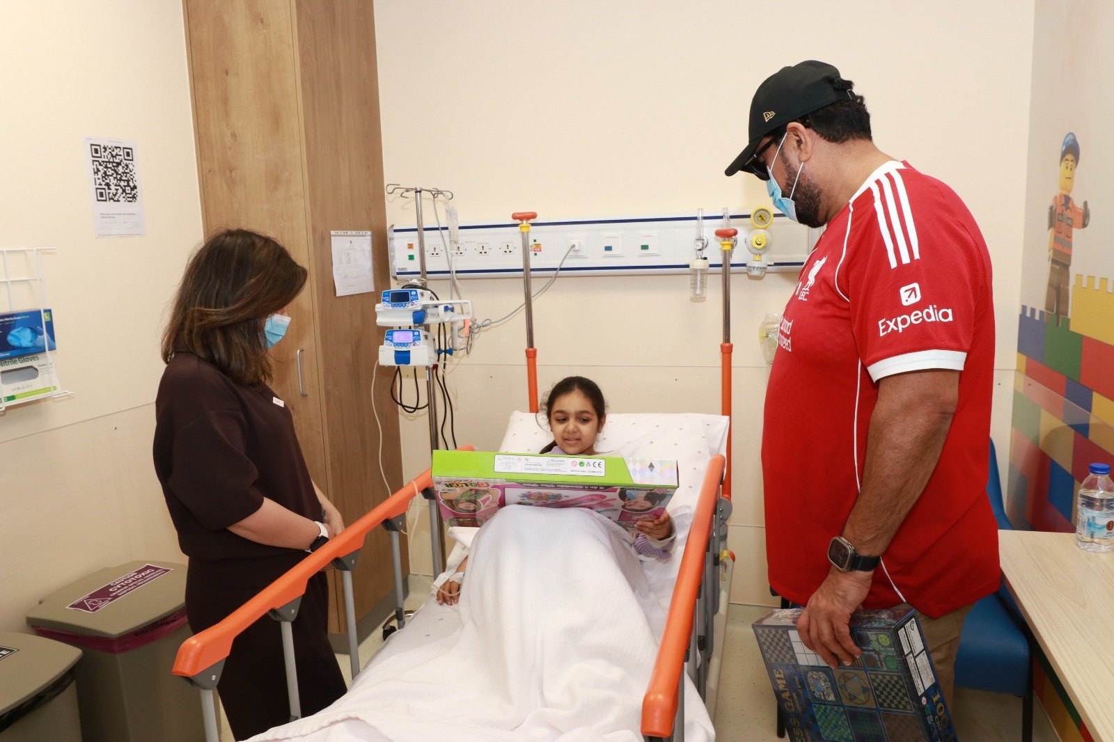 OLSC Bahrain representative presenting a gift to a child in a hospital room.