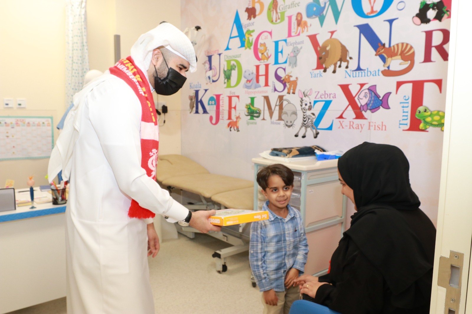 OLSC Bahrain representative offering a boxed gift to a child accompanied by an adult.